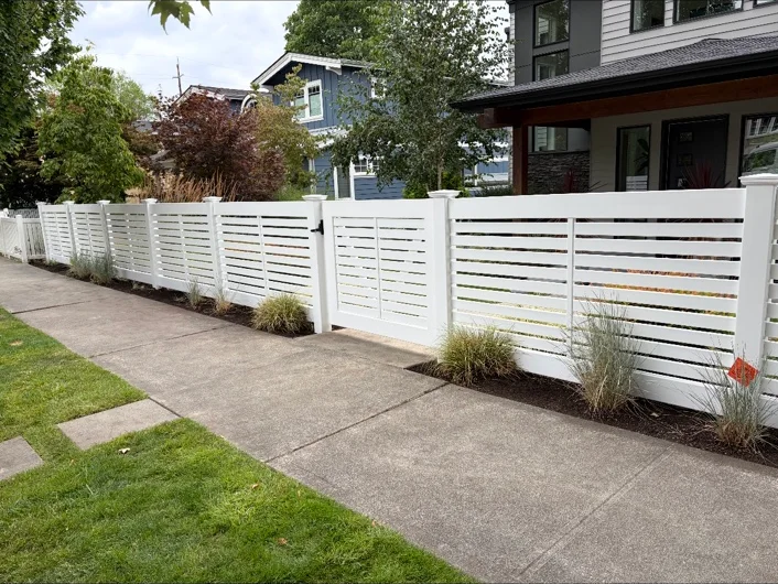 A completed Blue Ribbon white horizontal fence and matching gate outside a landscaped home.